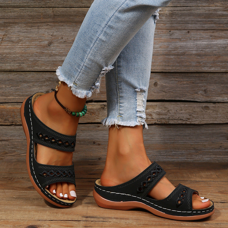 Woman wearing stylish black open-toe sandals with cutout design, paired with distressed light blue jeans, standing on wooden floor. Fashion footwear.