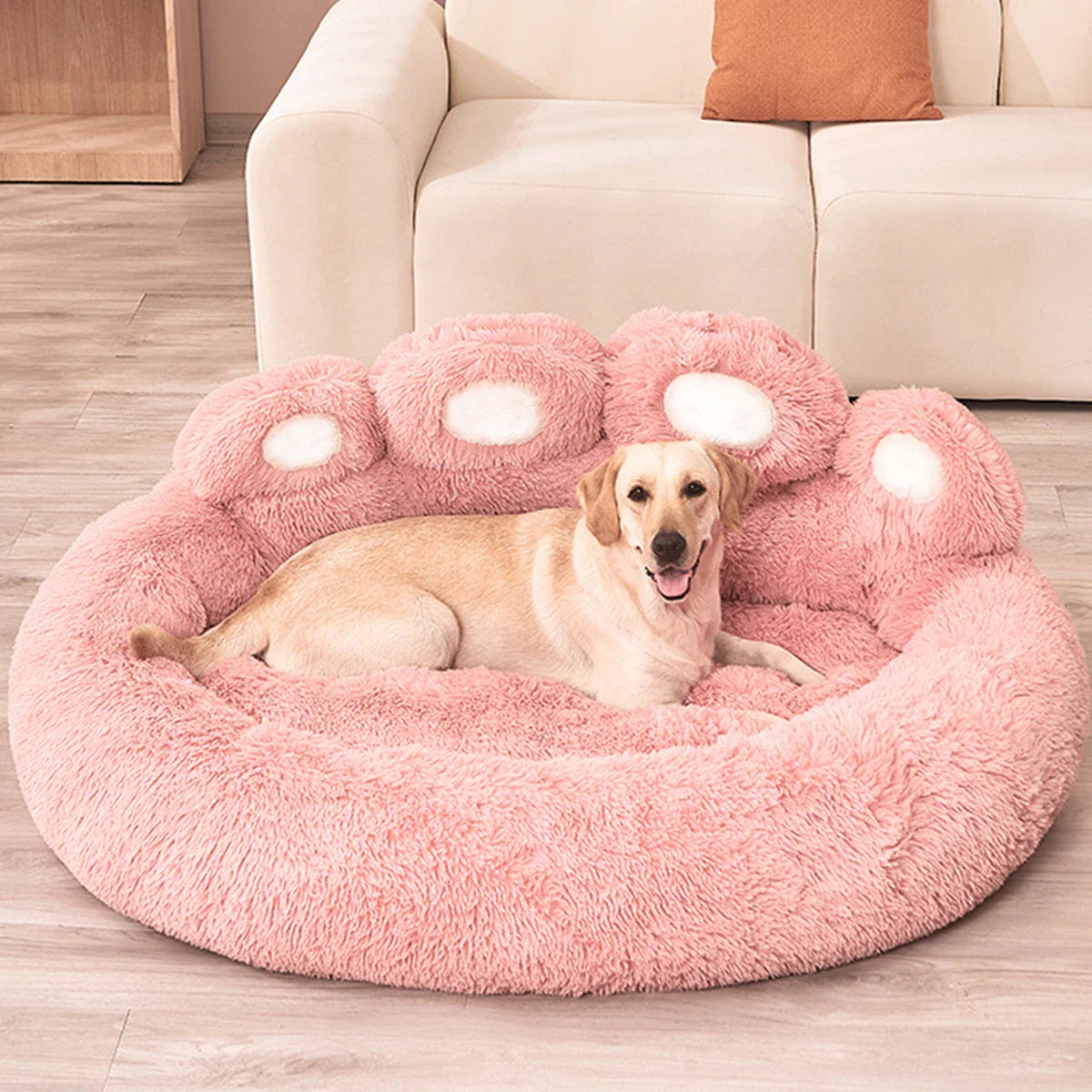 Dog resting on a large pink fluffy paw-shaped pet bed in a cozy living room setting.