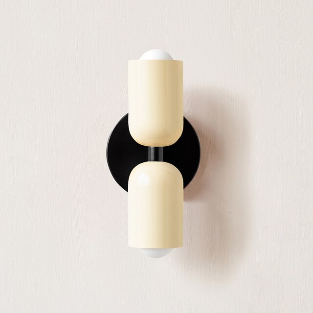 Modern wall sconce with dual cream cylindrical shades and black circular base, minimalist lighting fixture, contemporary home decor.