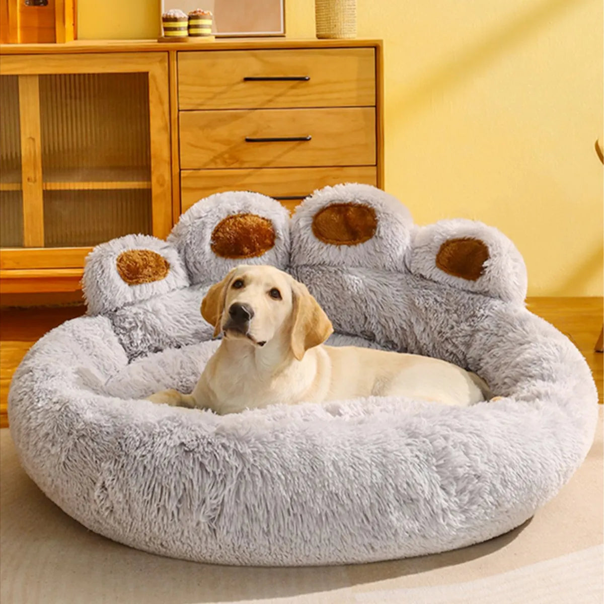 Fluffy gray dog bed shaped like a paw, with a Labrador retriever lying on it in a cozy room.