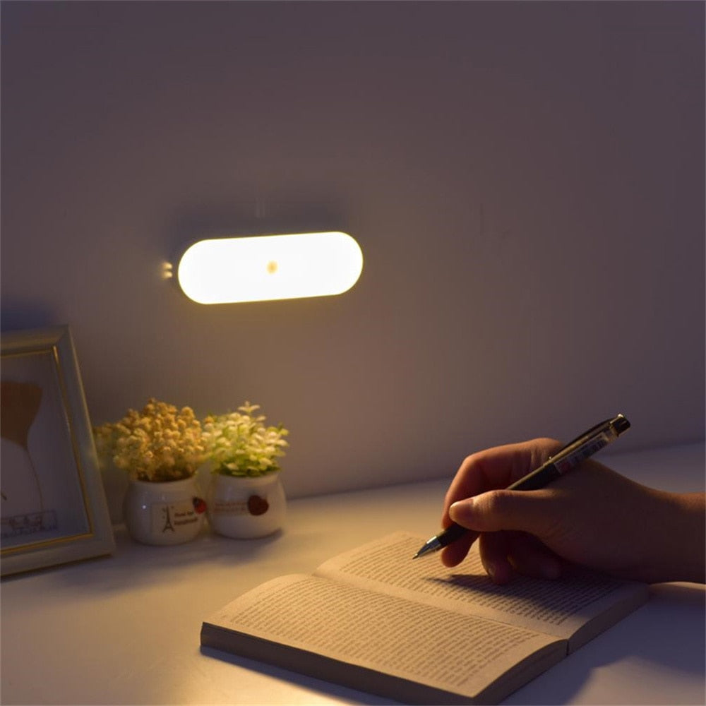 LED wall night light illuminating a desk with a person writing in a notebook, surrounded by small potted plants and a framed picture.