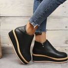 Black platform ankle boots with side zippers, worn with distressed blue jeans. Fashionable women's footwear, casual style, comfortable design.