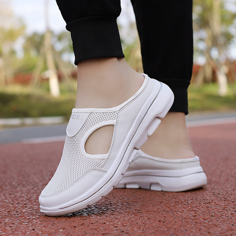 White slip-on athletic shoes with breathable mesh design, worn outdoors on a red track. Comfortable, lightweight footwear for walking or casual wear.