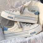 White canvas sneakers with blue accents, braided lace detail, and platform sole. Stylish casual footwear for women. Perfect for everyday wear.