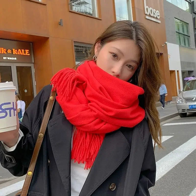 Woman in stylish black coat and vibrant red scarf holding a coffee cup on urban street. Fashionable winter outfit, city background, casual look.