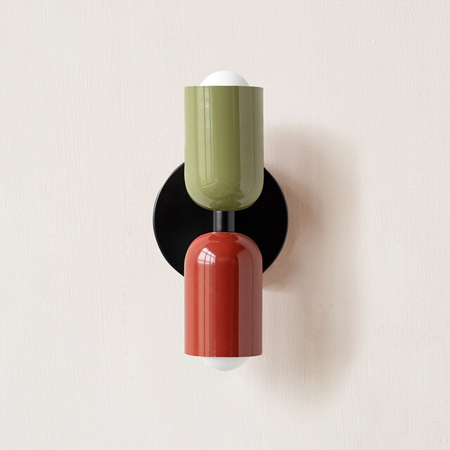 Modern wall sconce with dual-tone design, featuring green and red cylindrical shades on a black circular base. Contemporary home lighting fixture.