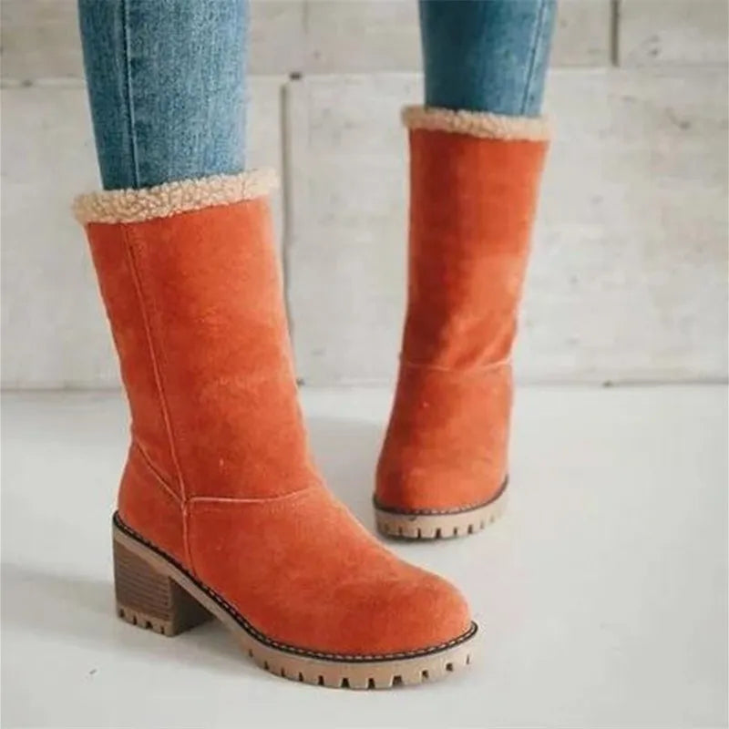 Orange suede winter boots with faux fur lining, block heel, and rugged sole, paired with blue jeans. Stylish women's footwear for cold weather.