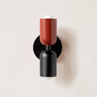 Modern wall sconce with red and black geometric design, featuring a minimalist style and dual light bulbs. Ideal for contemporary home lighting decor.