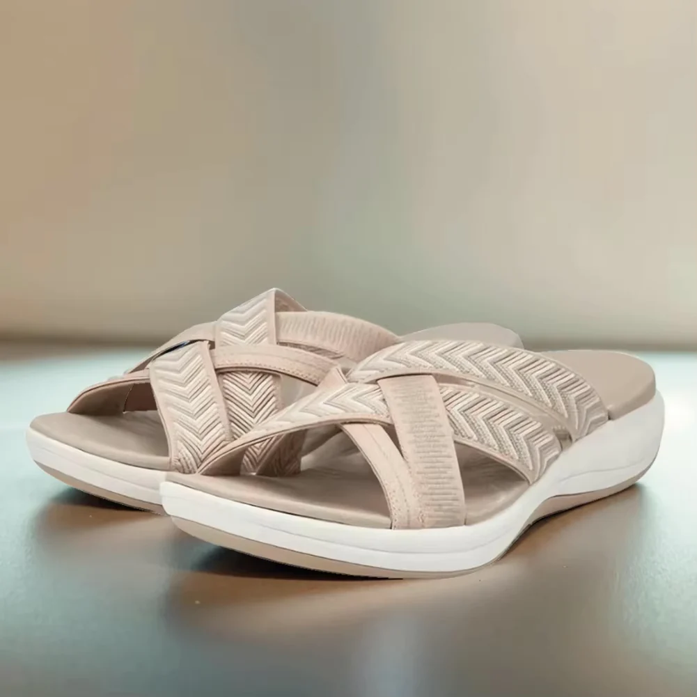 Beige women's slip-on sandals with crisscross straps and cushioned soles, featuring a chevron pattern. Comfortable summer footwear for casual wear.