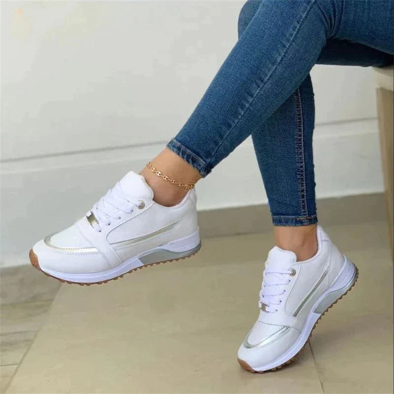 White women's sneakers with gold accents, worn with blue jeans, featuring a stylish design and comfortable fit. Perfect for casual wear and fashion-forward looks.