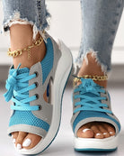 Women's blue mesh open-toe sneakers with white platform soles, gray accents, and gold anklets, paired with ripped jeans. Fashionable casual footwear.