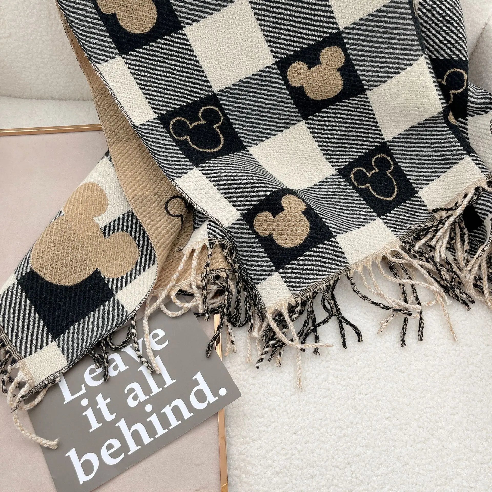 Plaid blanket with Mickey Mouse pattern and fringed edges on a white surface, accompanied by a sign reading "Leave it all behind." Cozy home decor.