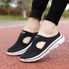 Black slip-on athletic walking shoes with breathable mesh design and white soles, worn outdoors on a red track.