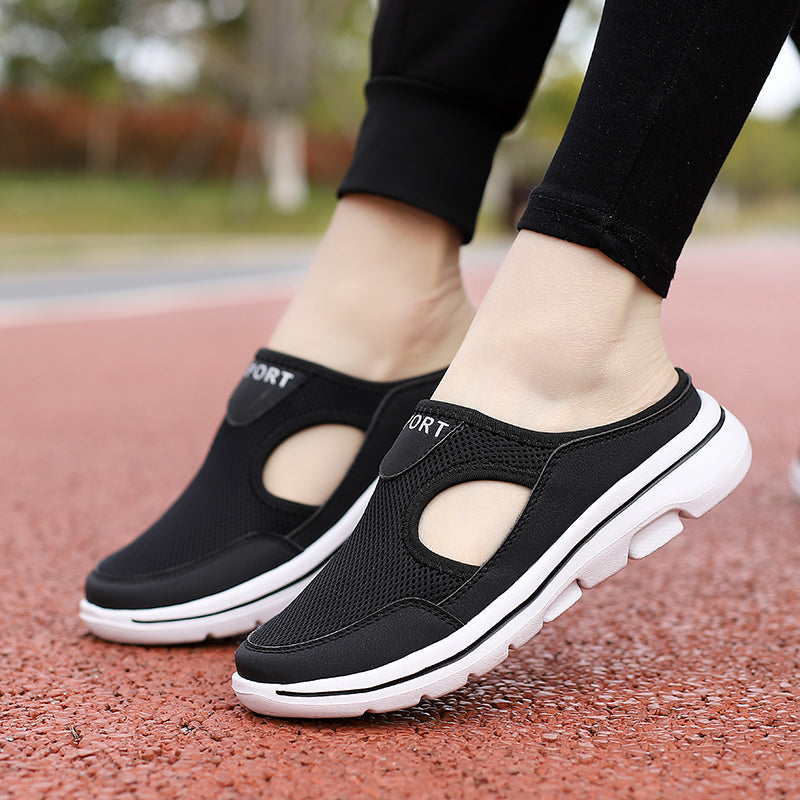 Black slip-on athletic walking shoes with breathable mesh design and white soles, worn outdoors on a red track.