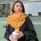 Woman in black coat and yellow scarf holding a coffee cup, standing by a green SUV. Fashionable autumn outfit, urban street style.