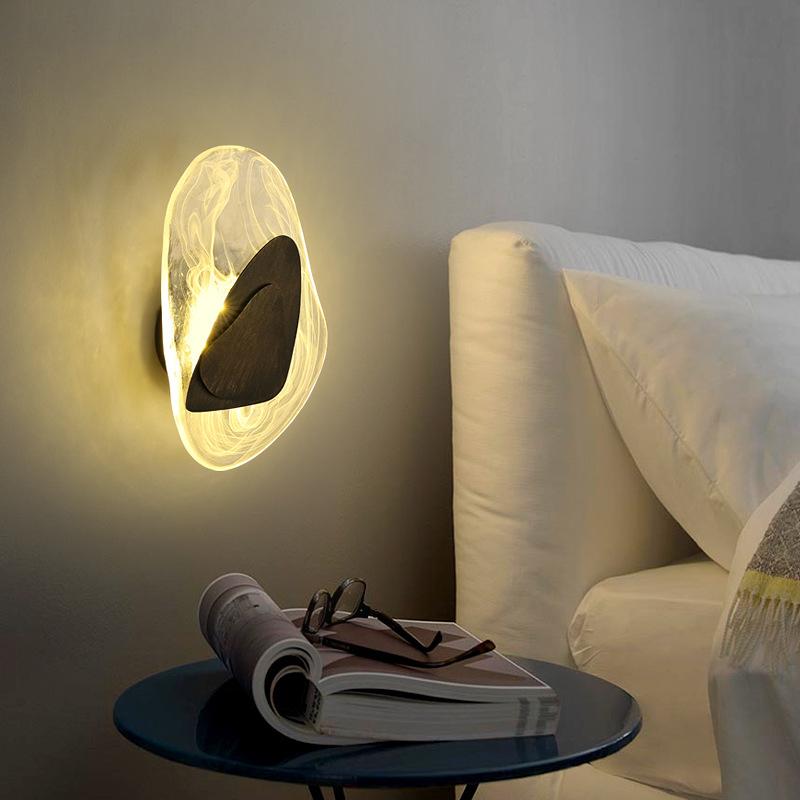 Modern wall sconce with abstract design, emitting warm ambient light, mounted beside a bed. Ideal for bedroom decor and contemporary lighting solutions.