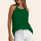 Woman wearing a sleeveless green pleated top with a round neckline, paired with white pants. Fashionable summer outfit, casual chic style.