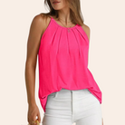 Woman wearing a vibrant pink sleeveless top with pleated neckline, paired with white jeans. Fashionable summer outfit, casual chic style.