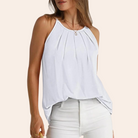 Woman wearing a sleeveless white pleated tank top paired with white jeans, showcasing casual summer fashion.