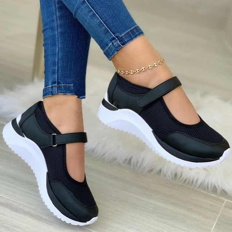 Black Mary Jane sneakers with white soles, worn with blue jeans, featuring a stylish ankle bracelet. Comfortable women's casual footwear.