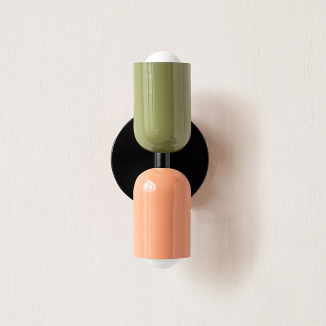 Modern wall sconce with green and peach cylindrical shades on a black base, minimalist lighting fixture, contemporary home decor.