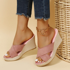 Women's pink wedge sandals with braided platform, open toe design, paired with frayed jeans and a heart anklet. Casual summer footwear.