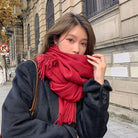 Woman in stylish black coat and red scarf on city street, autumn fashion, urban background, cozy winter outfit, trendy seasonal clothing.