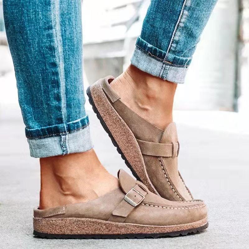 Beige suede slip-on clogs with buckle detail, worn with rolled-up blue jeans. Comfortable, stylish footwear for casual outings.