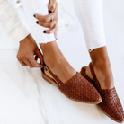 Woman wearing brown woven leather sandals with white jeans on a marble floor, adjusting strap. Stylish summer footwear, casual fashion.