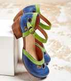 Blue and green vintage-style Mary Jane shoes with wooden heels, featuring cut-out details and a buckle strap, displayed on a textured surface.