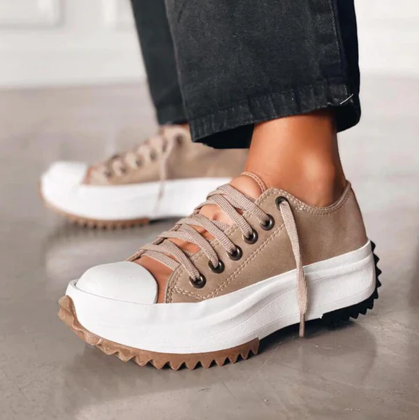 Trendy beige platform sneakers with white toe cap and chunky sole, worn with black pants. Fashionable footwear for casual style.