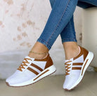 White and brown women's sneakers with perforated design, lace-up closure, and striped accents, paired with blue skinny jeans. Fashionable casual footwear.