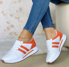 White and orange women's sneakers with perforated design, paired with blue jeans. Stylish casual footwear, perfect for everyday wear and comfort.