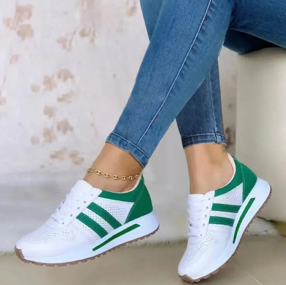 White and green athletic sneakers with perforated design, worn with blue jeans. Stylish casual footwear for women. Comfortable and trendy shoes.