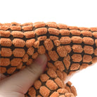 Close-up of a hand squeezing an orange microfiber chenille cleaning cloth with a textured, grid pattern, ideal for dusting and polishing surfaces.