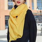 Woman wearing a bright yellow scarf over a black sweater, standing outdoors. Fashionable winter accessory, vibrant color contrast, urban background.