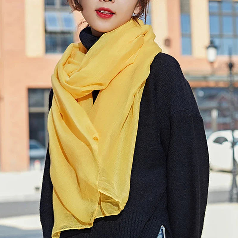 Woman wearing a bright yellow scarf over a black sweater, standing outdoors. Fashionable winter accessory, vibrant color contrast, urban background.