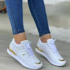 White women's sneakers with gold accents, quilted design, and heart detail, paired with blue jeans. Fashionable casual footwear for women.