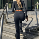 Woman in black activewear climbing outdoor stairs, showcasing fitness fashion. Urban background, long sleeves, leggings, modern workout attire.
