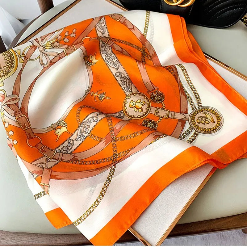 Elegant orange silk scarf with intricate equestrian print, featuring gold chains and buckles, displayed on a chair. Fashion accessory, luxury style.
