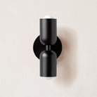 Modern black wall sconce with dual cylindrical lights on a round base, minimalist design, ideal for contemporary home lighting decor.