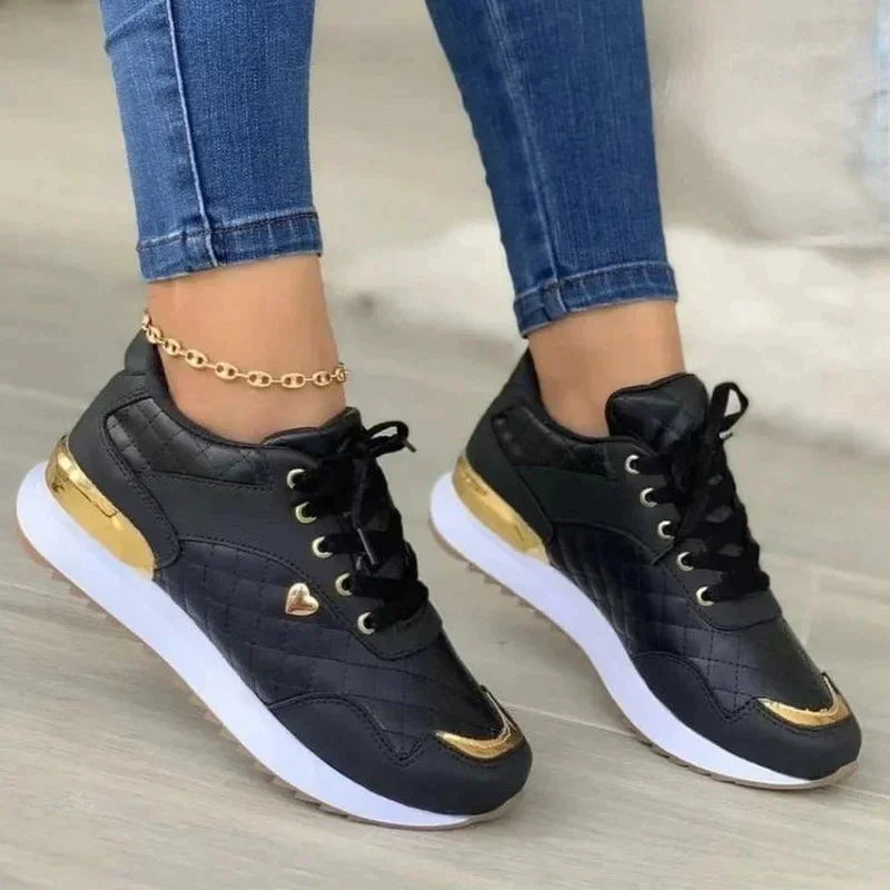 Black and gold women's sneakers with quilted design, white soles, and heart detail, paired with blue jeans. Stylish casual footwear for women.