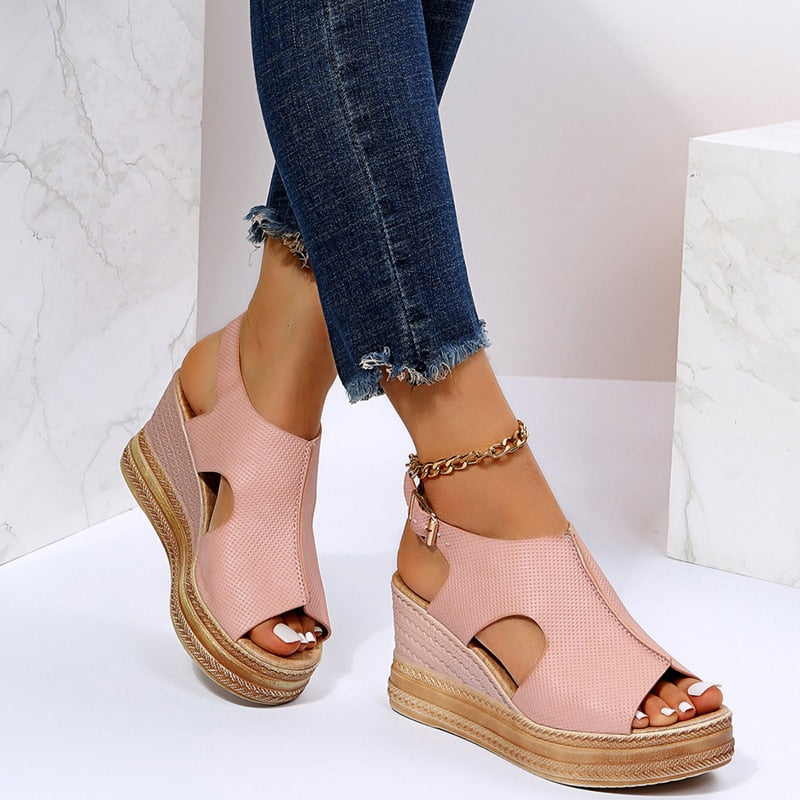 Pink wedge sandals with cutout design and ankle strap, paired with frayed hem blue jeans. Fashionable summer footwear for women.