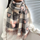 Plaid scarf with pink and gray Mickey Mouse pattern, worn by a person in a white sweater, featuring fringe details. Cozy winter fashion accessory.