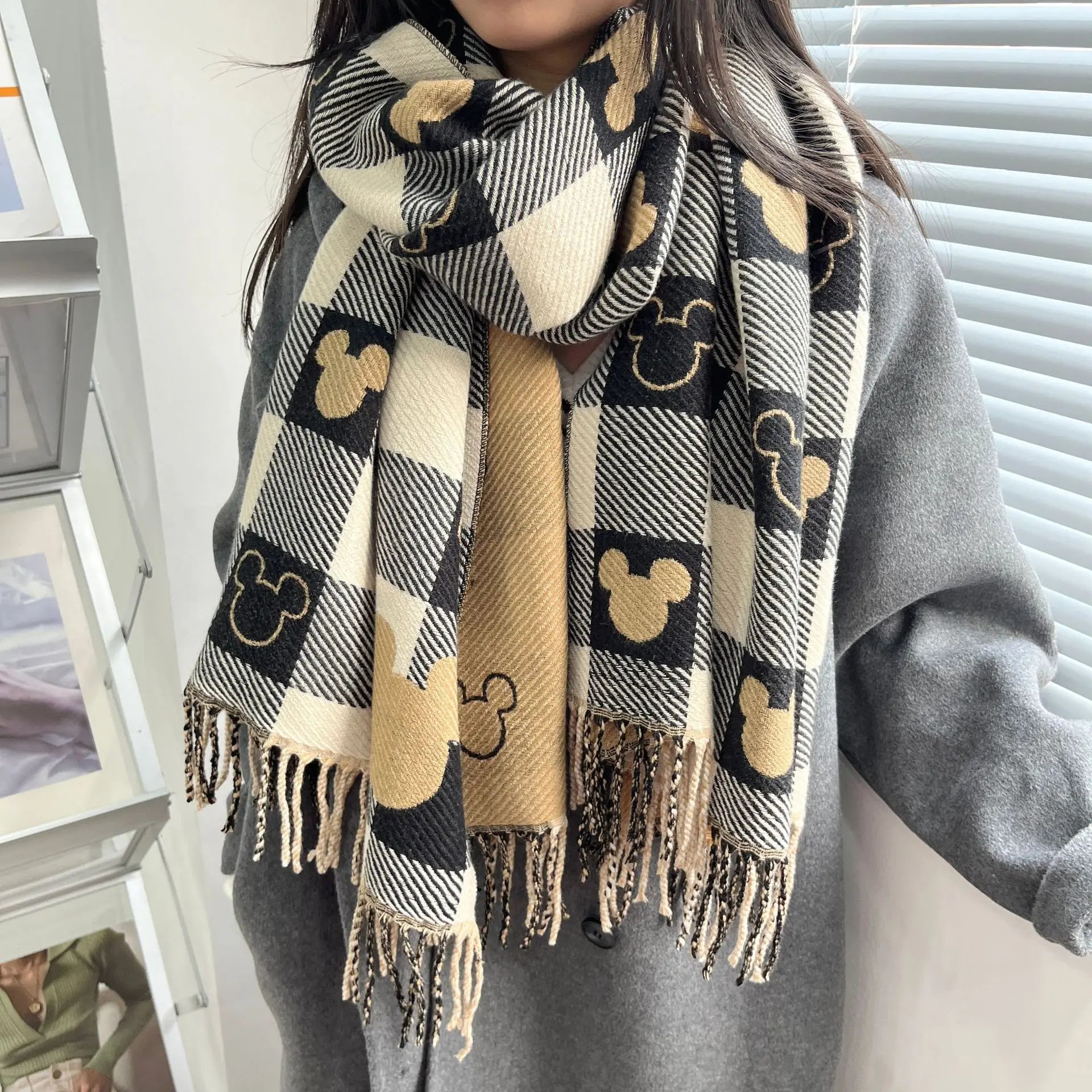 Stylish plaid scarf with Mickey Mouse pattern, featuring black, beige, and white colors. Perfect winter accessory for Disney fans. Cozy and trendy.