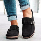 Women's retro slip-on mules in black suede with buckle detail, paired with rolled-up jeans. Comfortable, casual flats, plus size available.