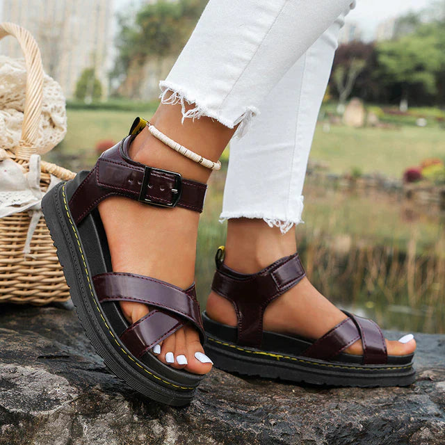 Women's brown Roman platform sandals with adjustable buckle, worn with white jeans. Perfect for summer fashion and outdoor casual style.