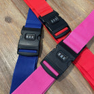 Colorful luggage straps with combination locks on wooden surface; red, blue, and pink travel accessories for secure baggage handling.