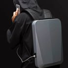 Sleek anti-theft backpack with USB charging port, worn by person in black hoodie using smartphone. Modern, secure travel gear for tech-savvy users.