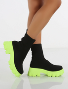 Black sock boots with neon green chunky platform soles, women's fashion footwear, trendy ankle boots, stylish statement shoes, modern design.